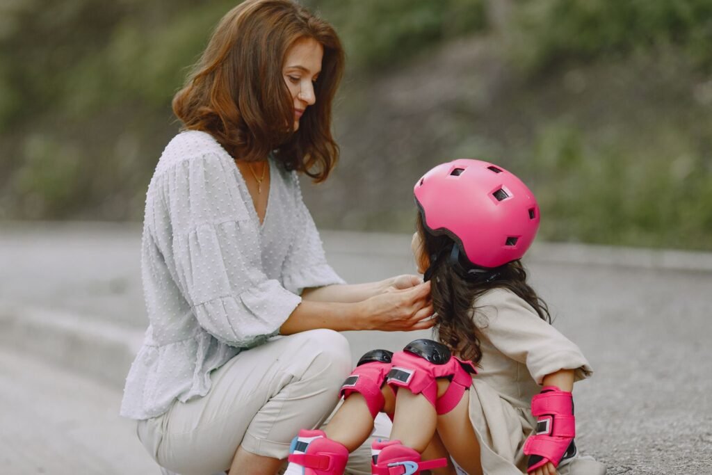 Mother helping her daughter put on a pink helmet and knee pads